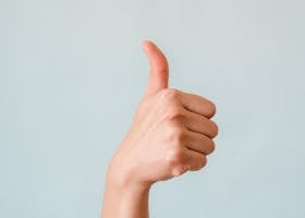 Close-up of a hand showing a thumbs up gesture on a blue background.